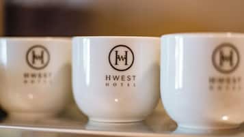 Three white ceramic cups with the logo and name of the HWEST Hotel.