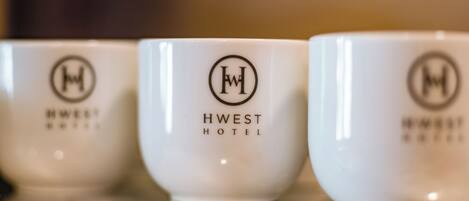 Tre tazze di ceramica bianca con il logo e il nome dell'Hotel HWEST.