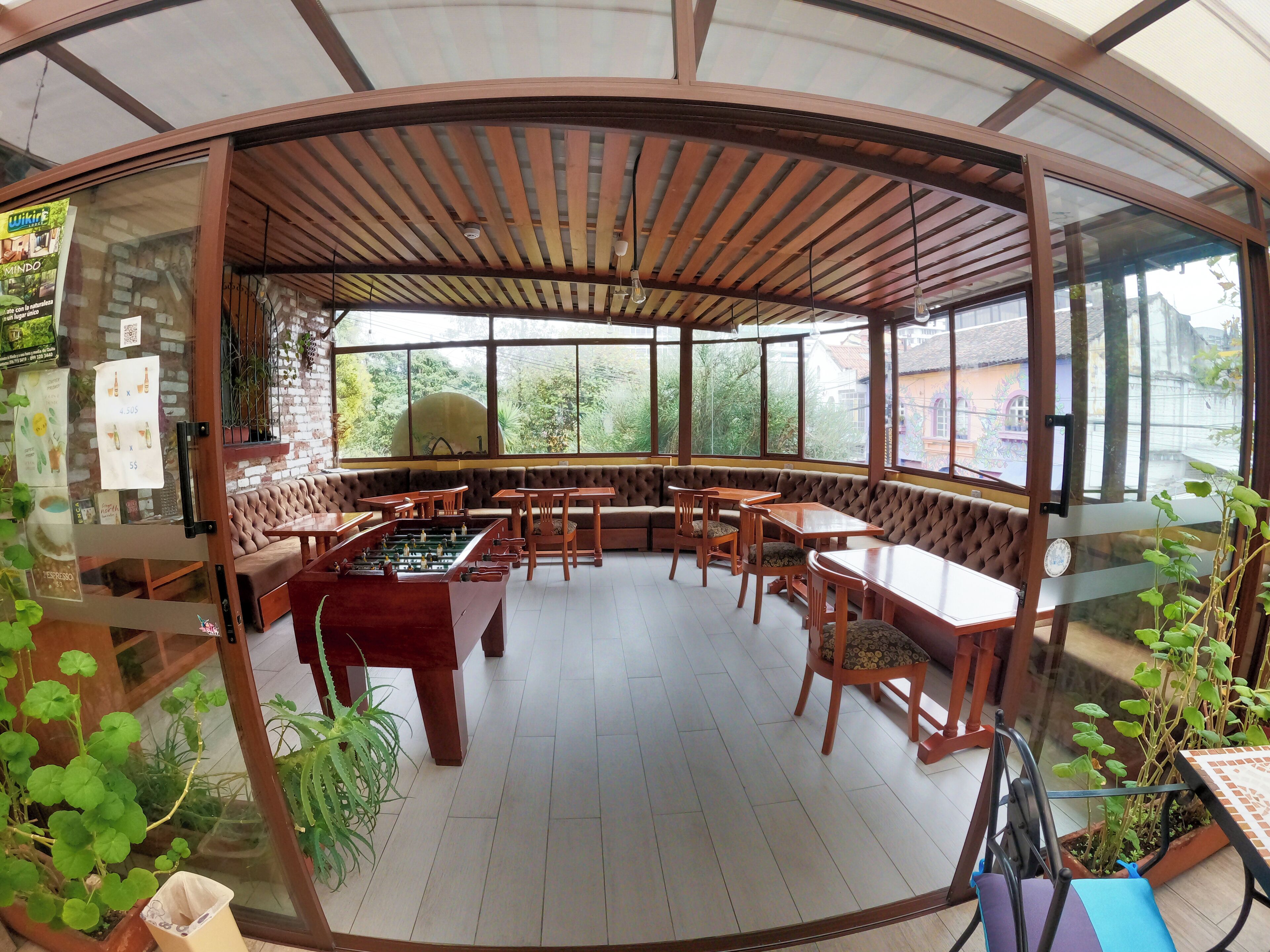 Un espace intérieur accueillant avec des tables et des chaises en bois, un baby-foot et de grandes fenêtres donnant sur un paysage verdoyant.