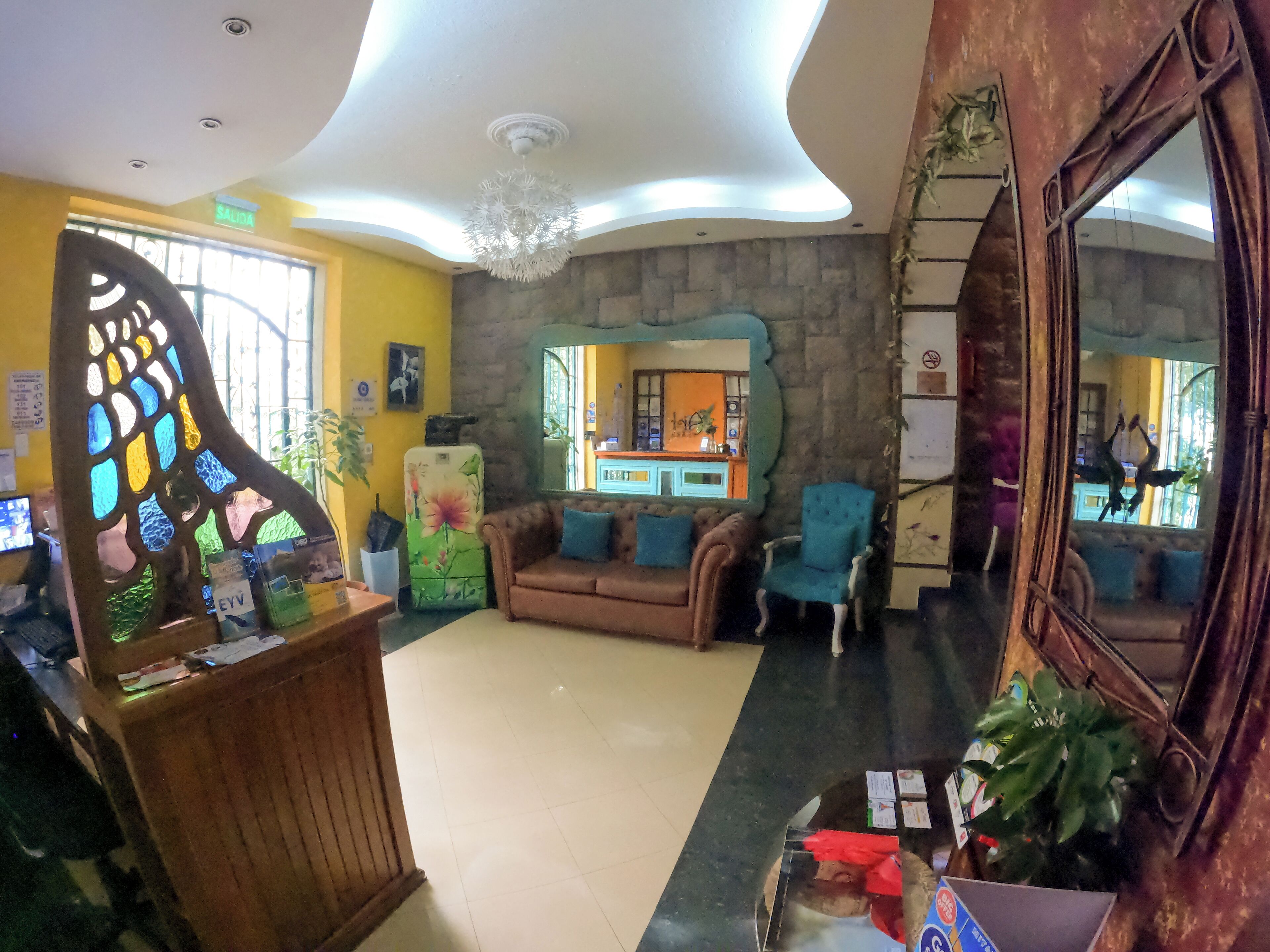 A lobby with a reception desk, a sofa, and a chair. There is a refrigerator with a floral design, a mirror, and a window with bars.