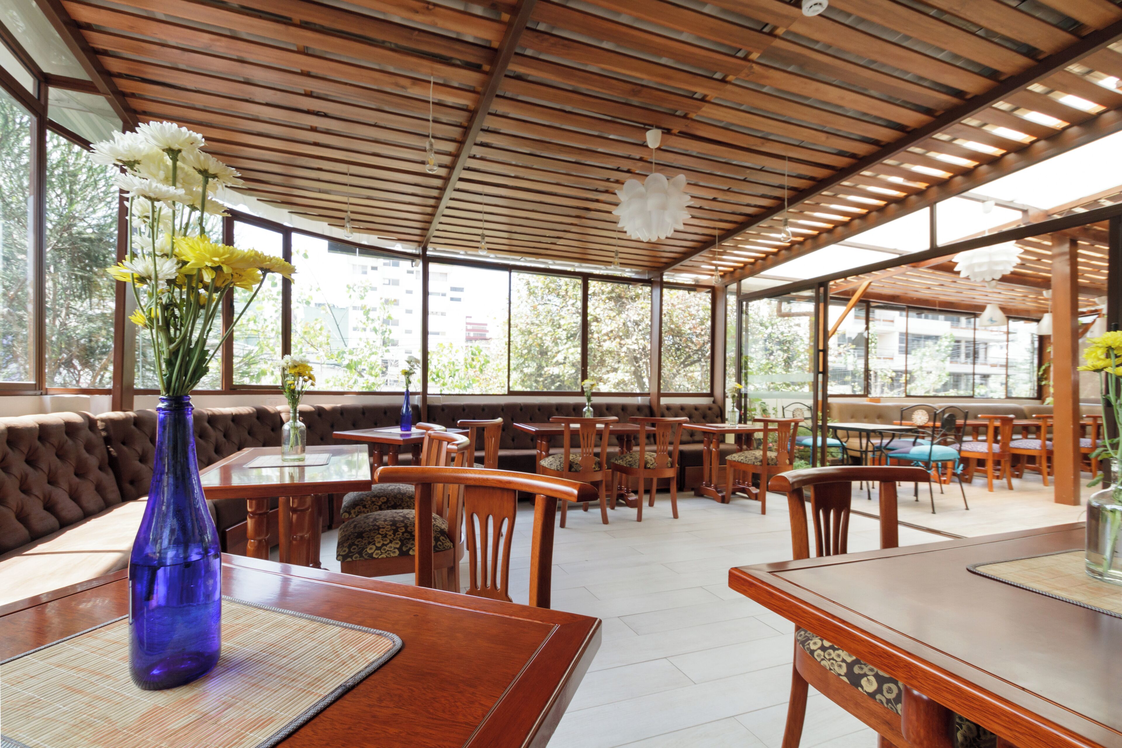 Un restaurante con mesas y sillas de madera, un banco acolchado y ventanas grandes.