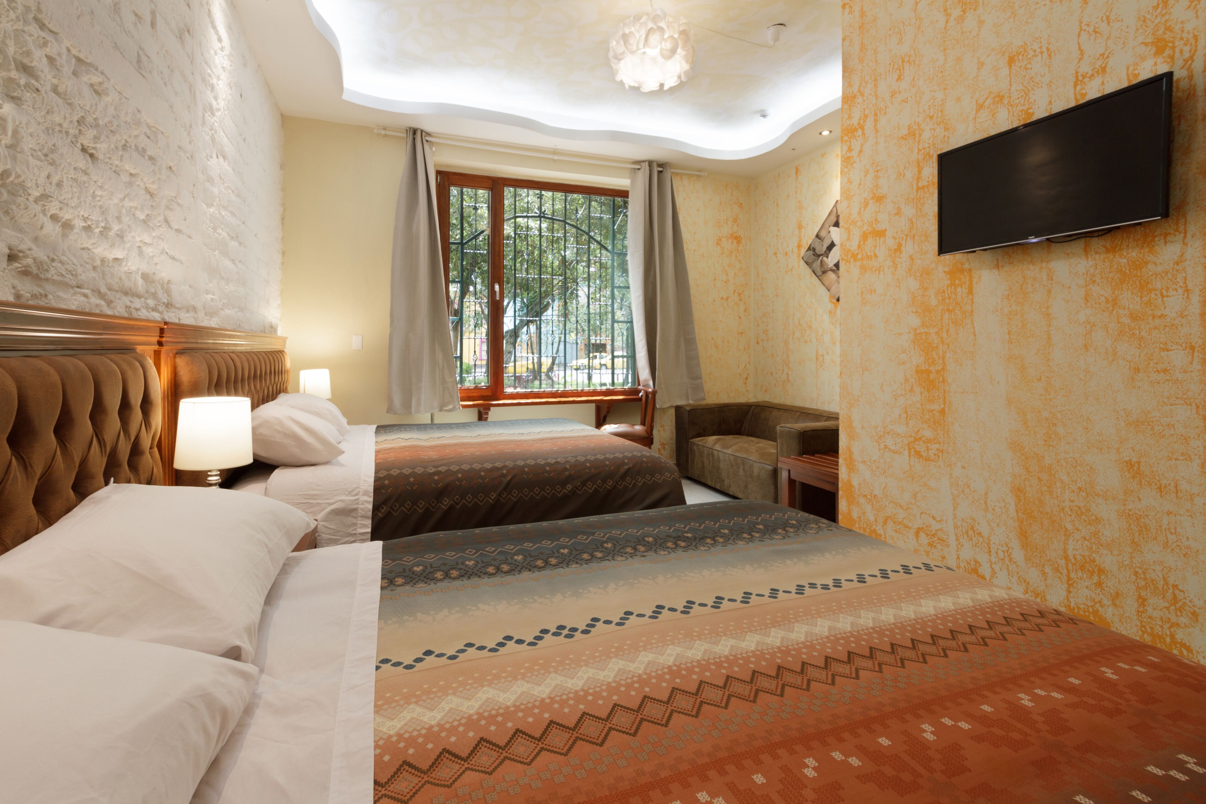 Ein Hotelzimmer mit zwei Betten, einem Fernseher, einem Fenster mit Vorhängen und Blick auf Grün.