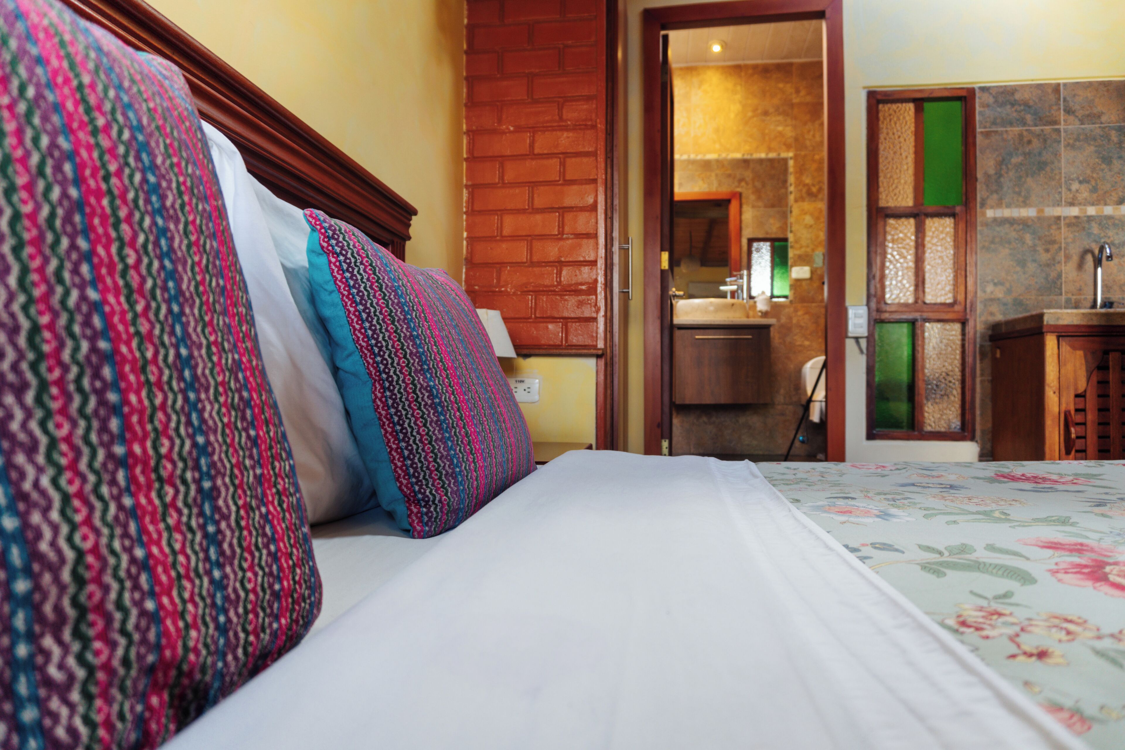 A hotel room with a bed, pillows, a desk, and a bathroom visible through an open door.