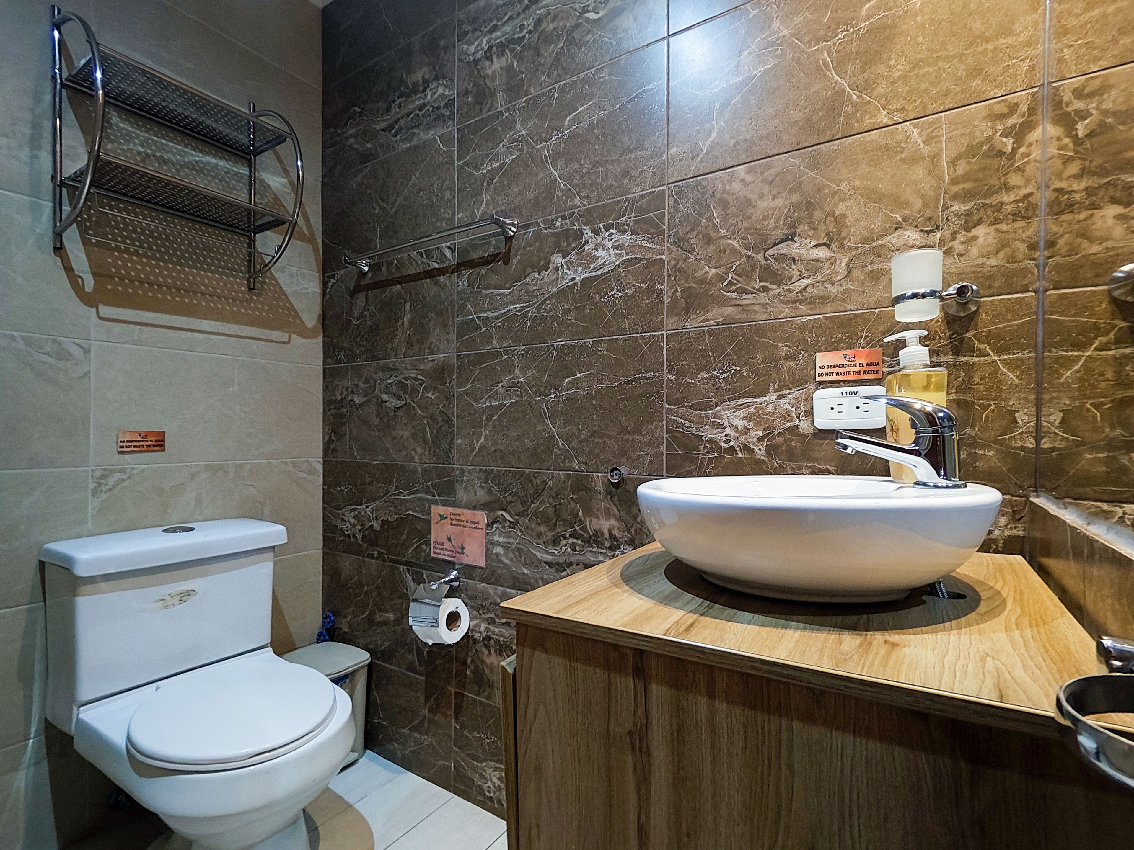 Un baño con inodoro blanco, lavamanos con espejo y un perchero para toallas.