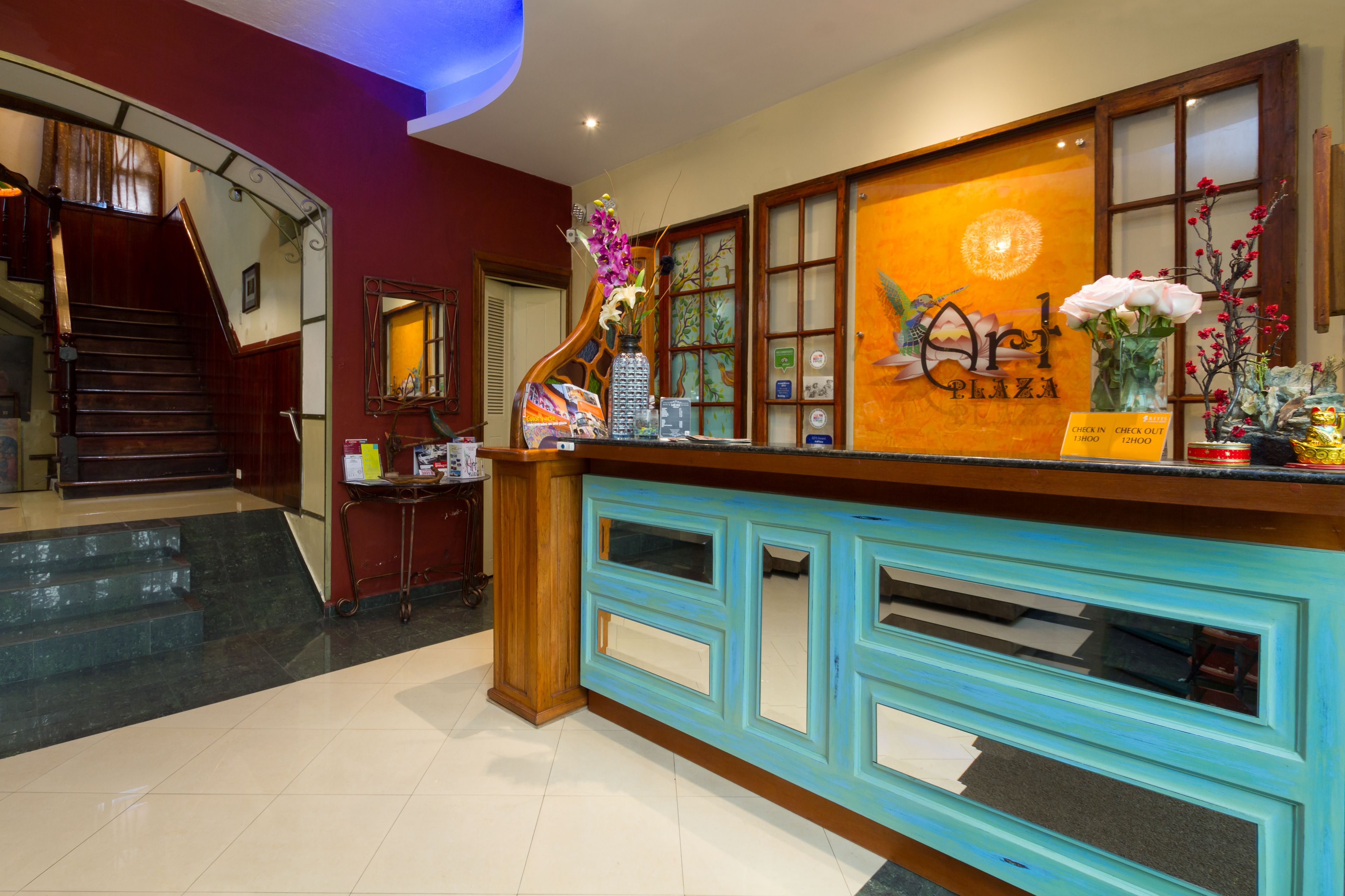 A reception desk with a wooden finish and a blue accent, a staircase, and a wall with a floral arrangement and a sign reading "Orch Plaza".