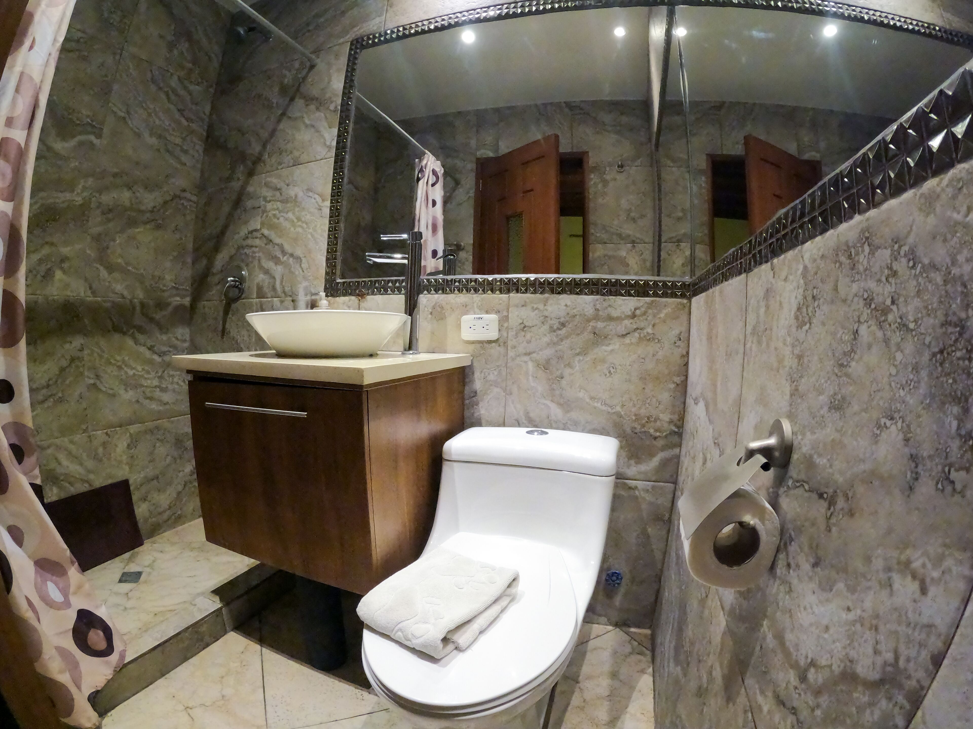 Un bagno con parete in marmo, lavabo, WC e specchio con cornice decorativa.