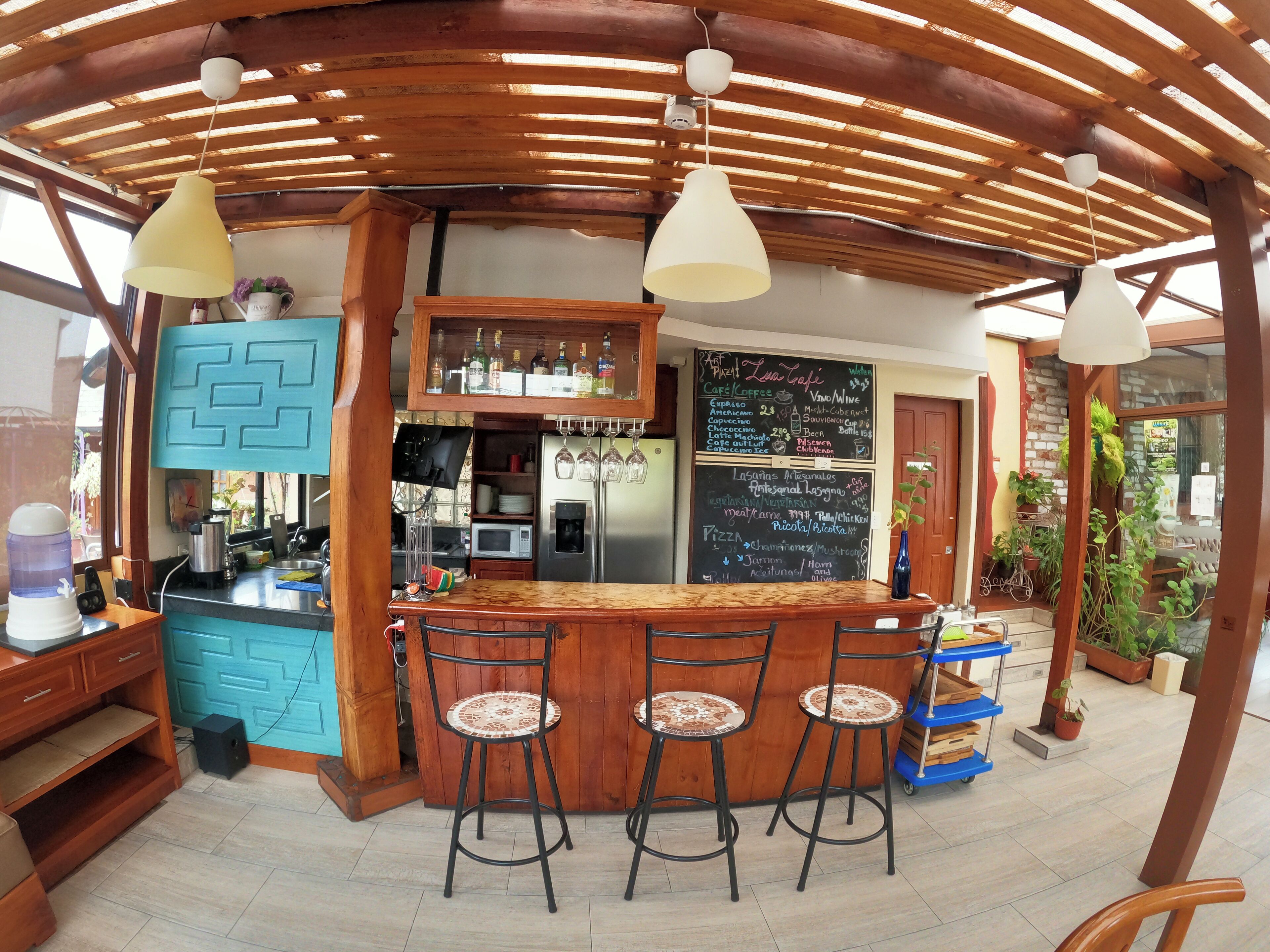 A bar area with a wooden ceiling, bar stools, a counter with a chalkboard menu, and a refrigerator.