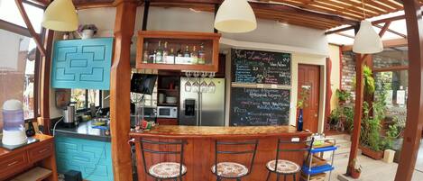 A bar area with a wooden ceiling, bar stools, a counter with a chalkboard menu, and a refrigerator.