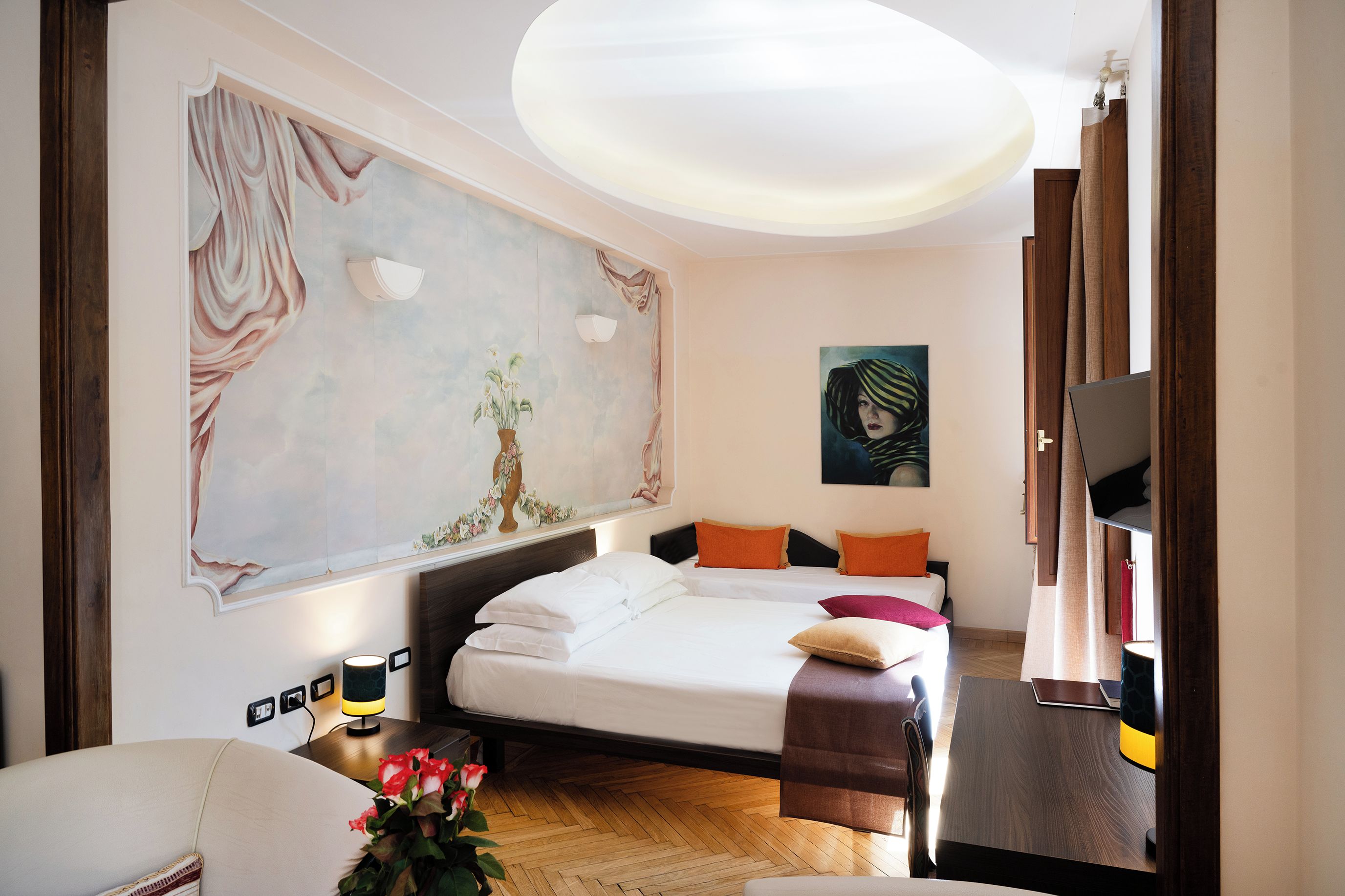 Una camera d'albergo con un letto, una scrivania, una TV e un grande quadro appeso al muro.