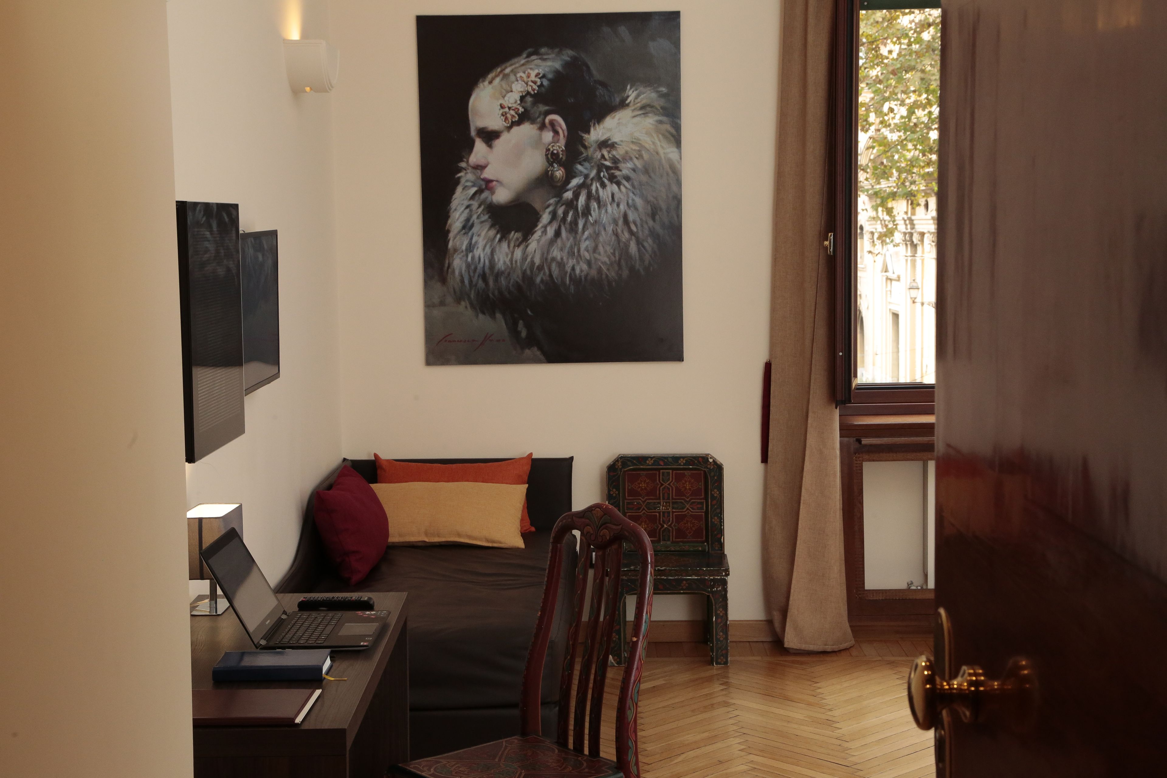 Een slaapkamer met een bed, een bureau met een laptop, een stoel, een klein tafeltje en een raam met gordijnen.
