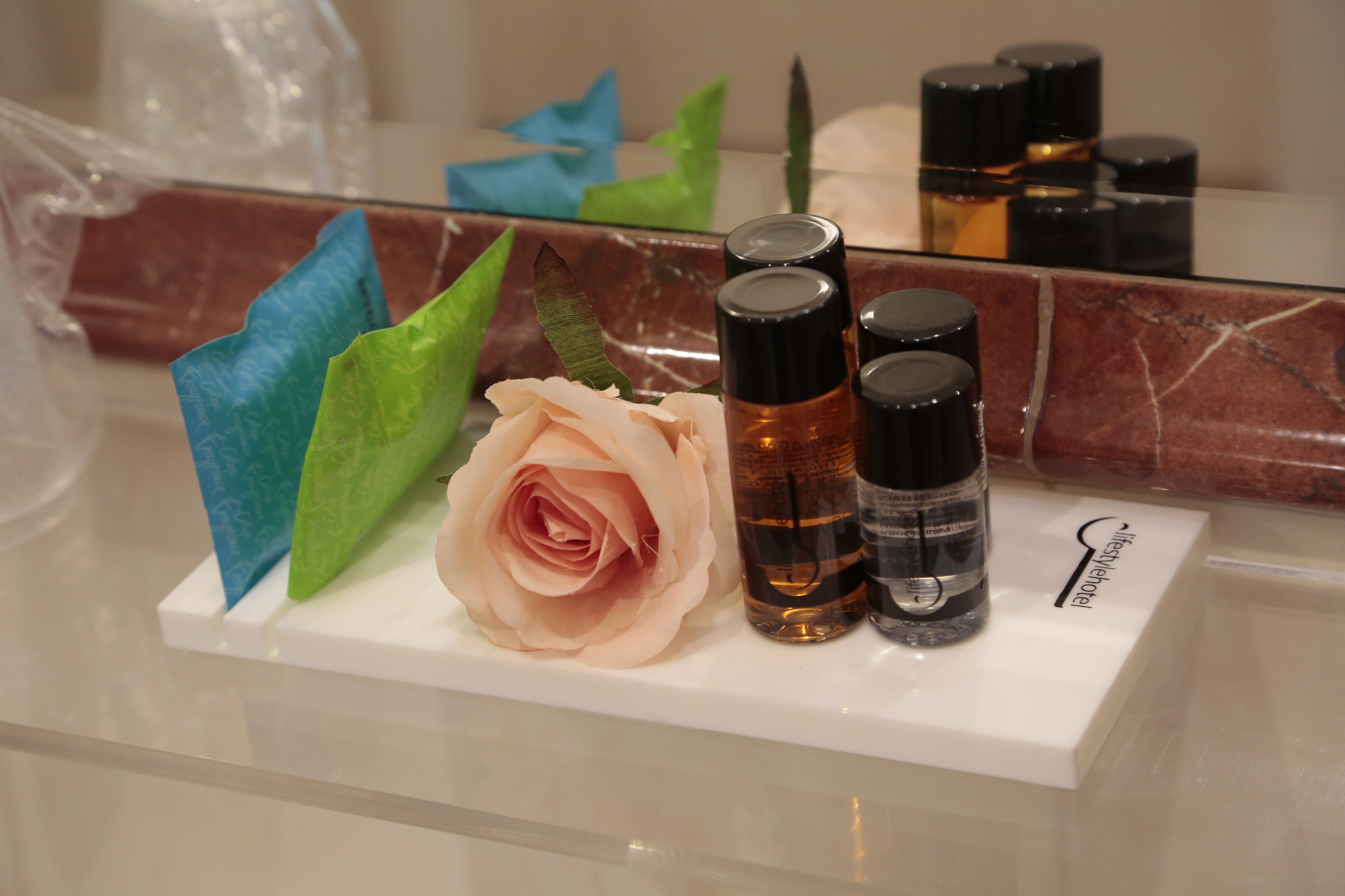 Un comptoir de salle de bain avec une rose, un mouchoir bleu et trois bouteilles de liquide.