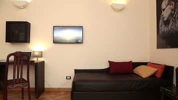 A room with a black sofa, a wooden chair, a desk with a lamp, and a wall-mounted TV.