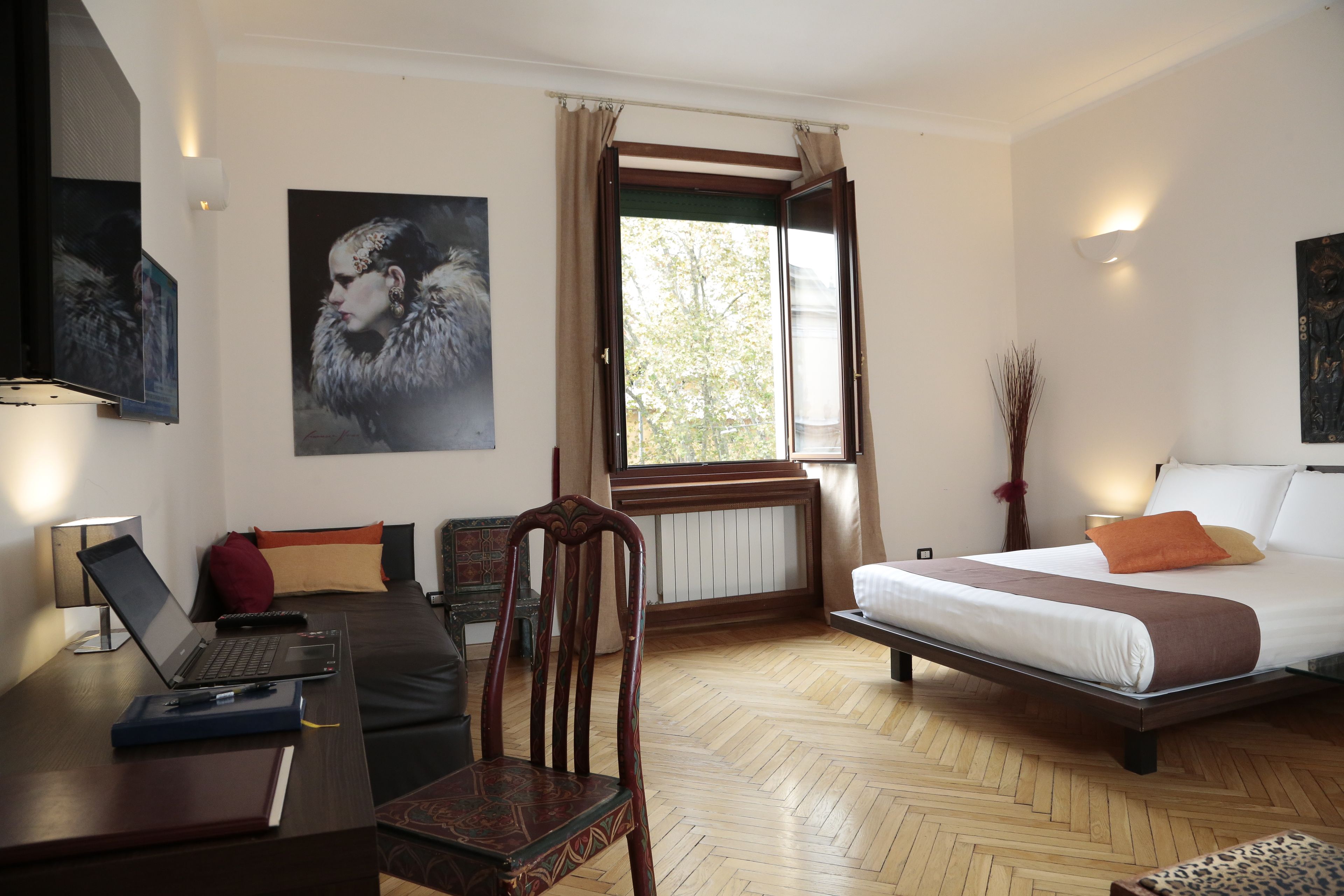 Ett hotellrum med en säng, ett skrivbord med en bärbar dator, en stol och ett fönster med gardiner.