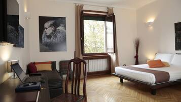 Ett hotellrum med en säng, ett skrivbord med en bärbar dator, en stol och ett fönster med gardiner.