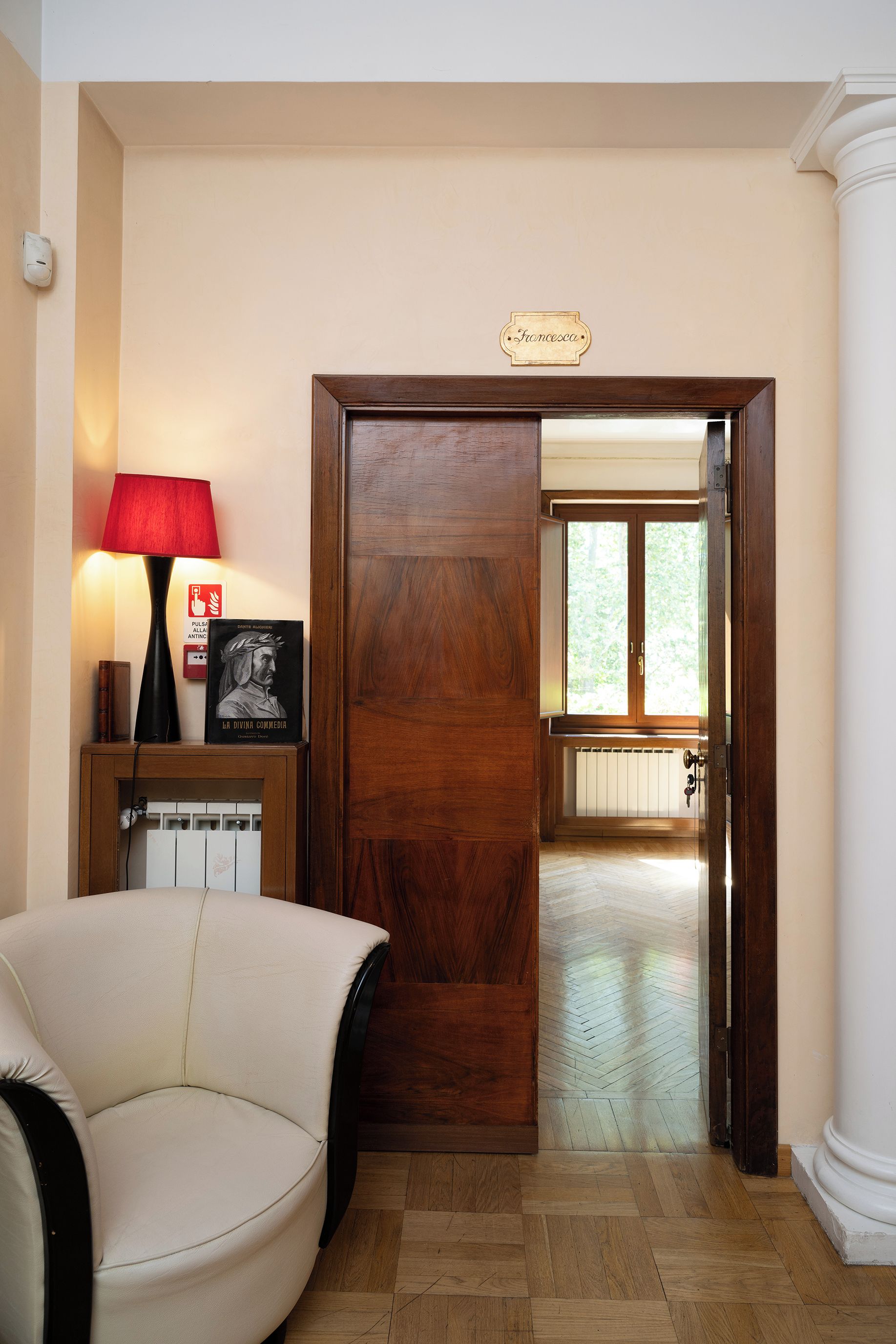 Een kamer met een houten deur, een rode lamp, een lijst met een afbeelding en een radiator.