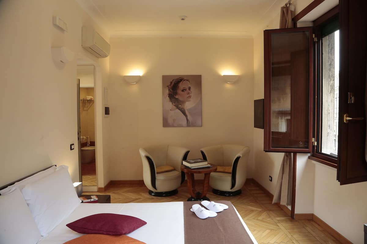 Een hotelkamer met een bed, twee fauteuils, een bijzettafeltje en een schilderij aan de wand.