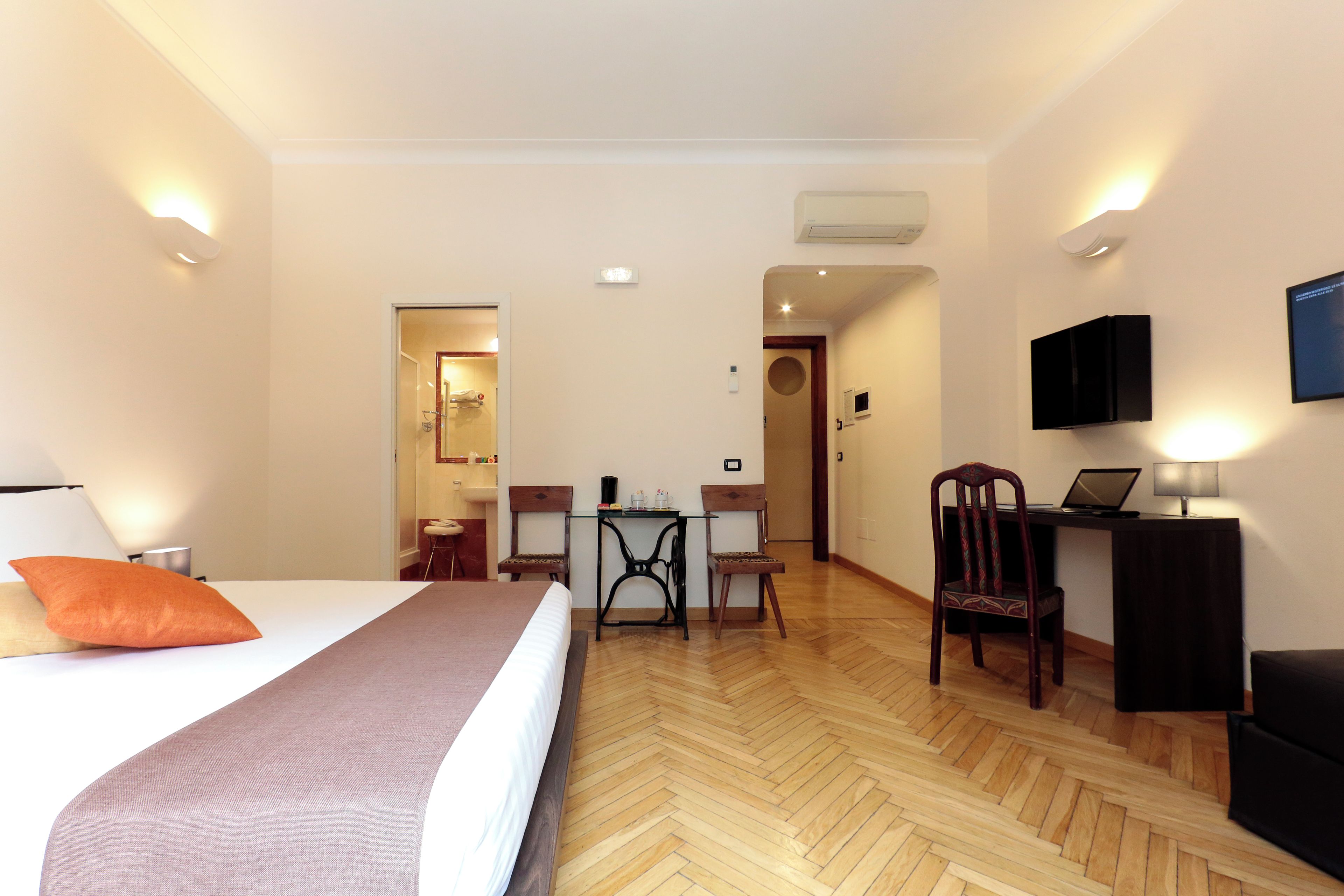 A hotel room with a bed, a desk, a chair, a television, and a laptop.