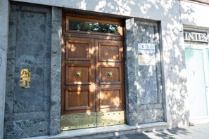 Una puerta de madera grande con un tirador de bronce, ubicada en una pared de piedra con una placa metálica y un cartel arriba.