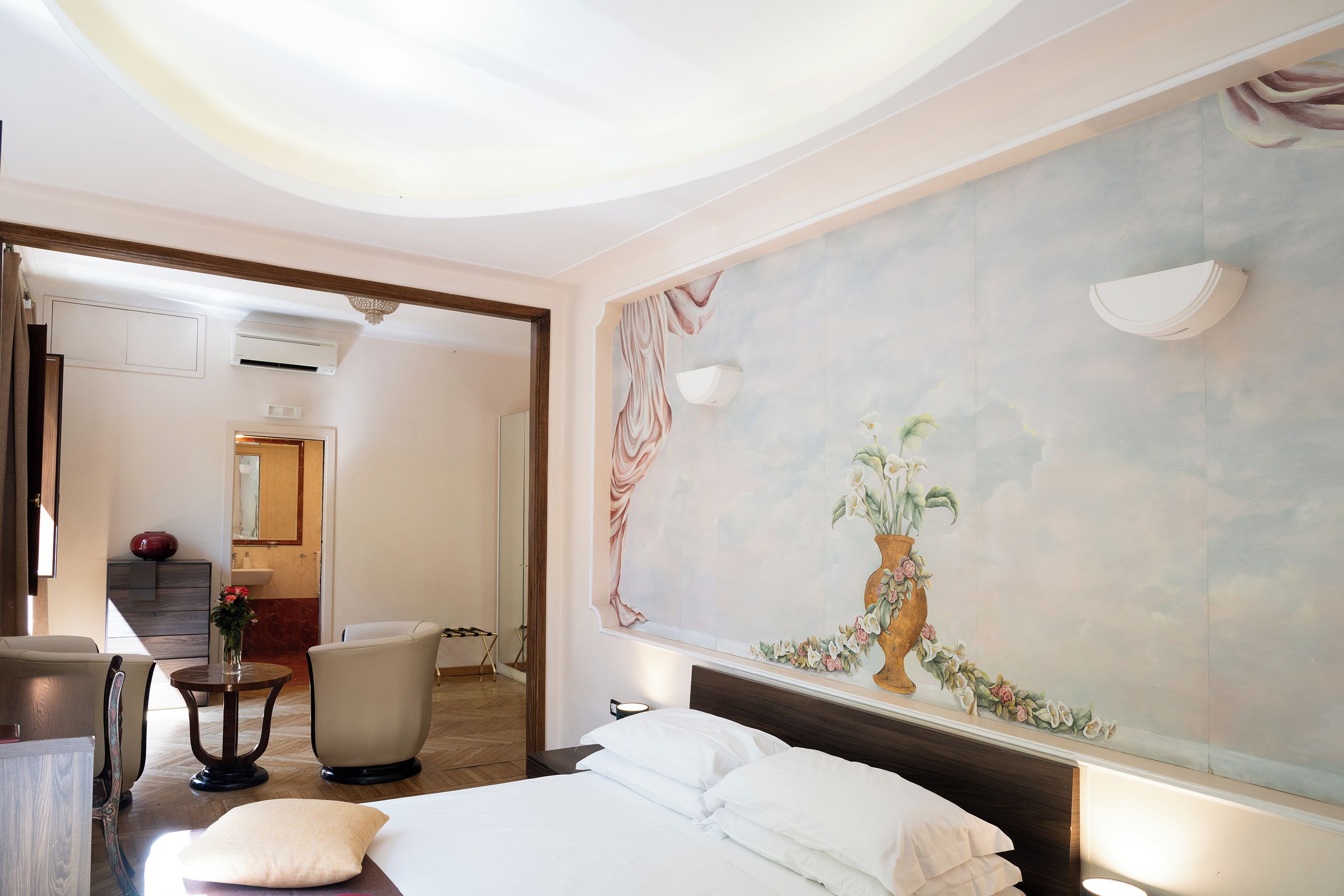 Una camera d'albergo con un letto, una sedia, una scrivania e un bagno visibile attraverso una porta aperta.