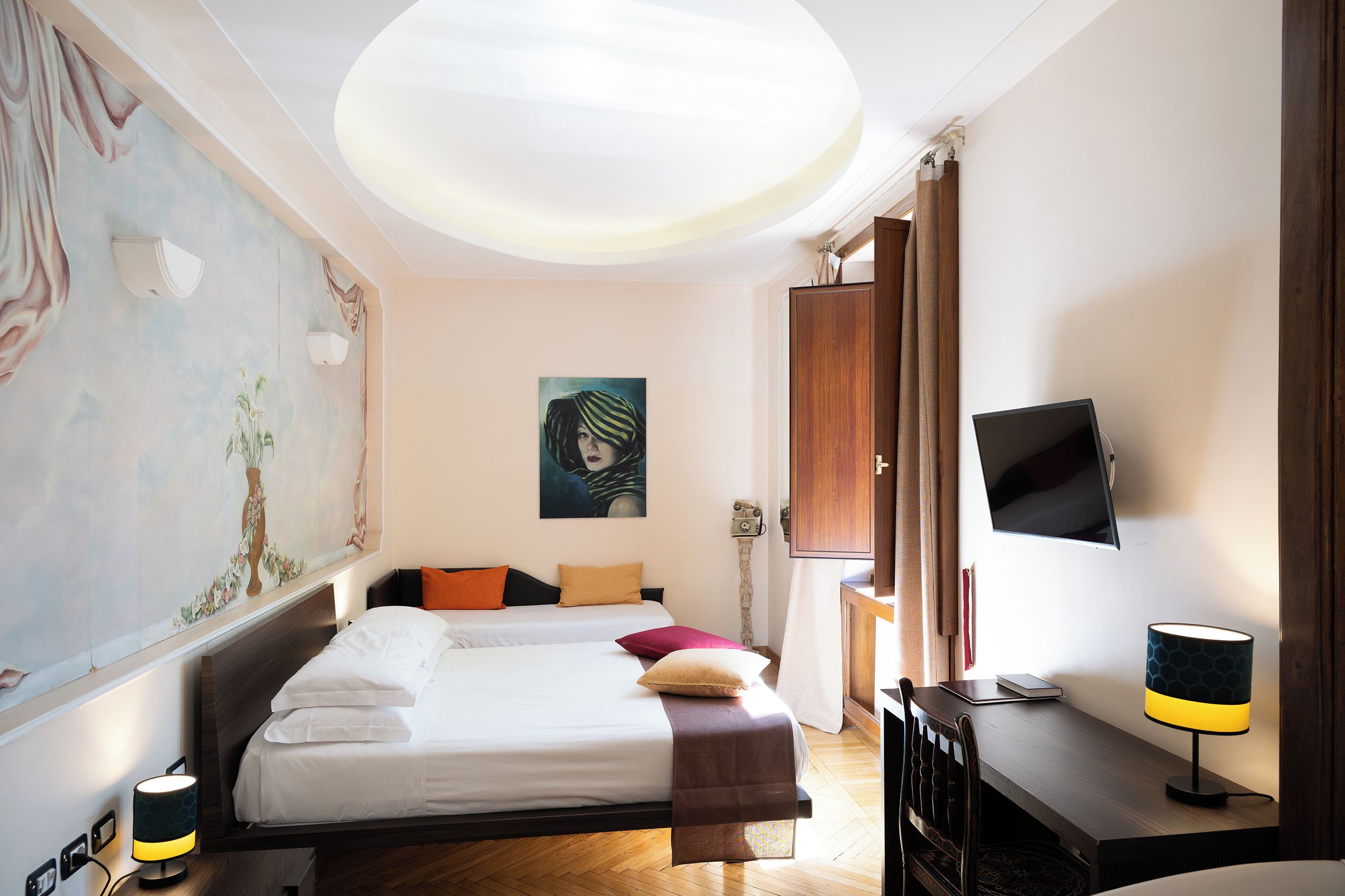 Une chambre d’hôtel avec un lit, un bureau, une télévision et un grand tableau au mur.