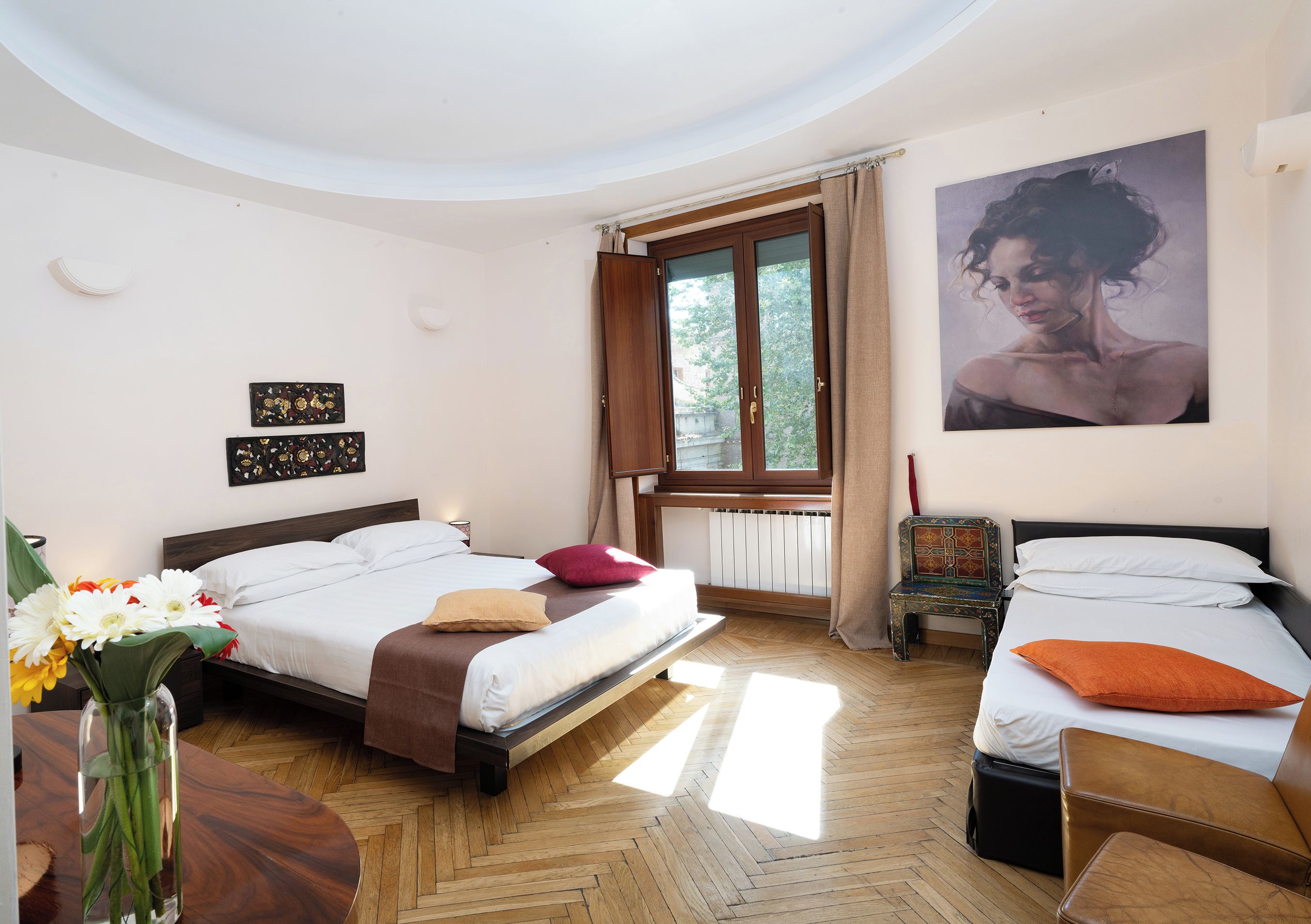 A hotel room with two beds, a window with curtains, a painting on the wall, and a wooden floor.