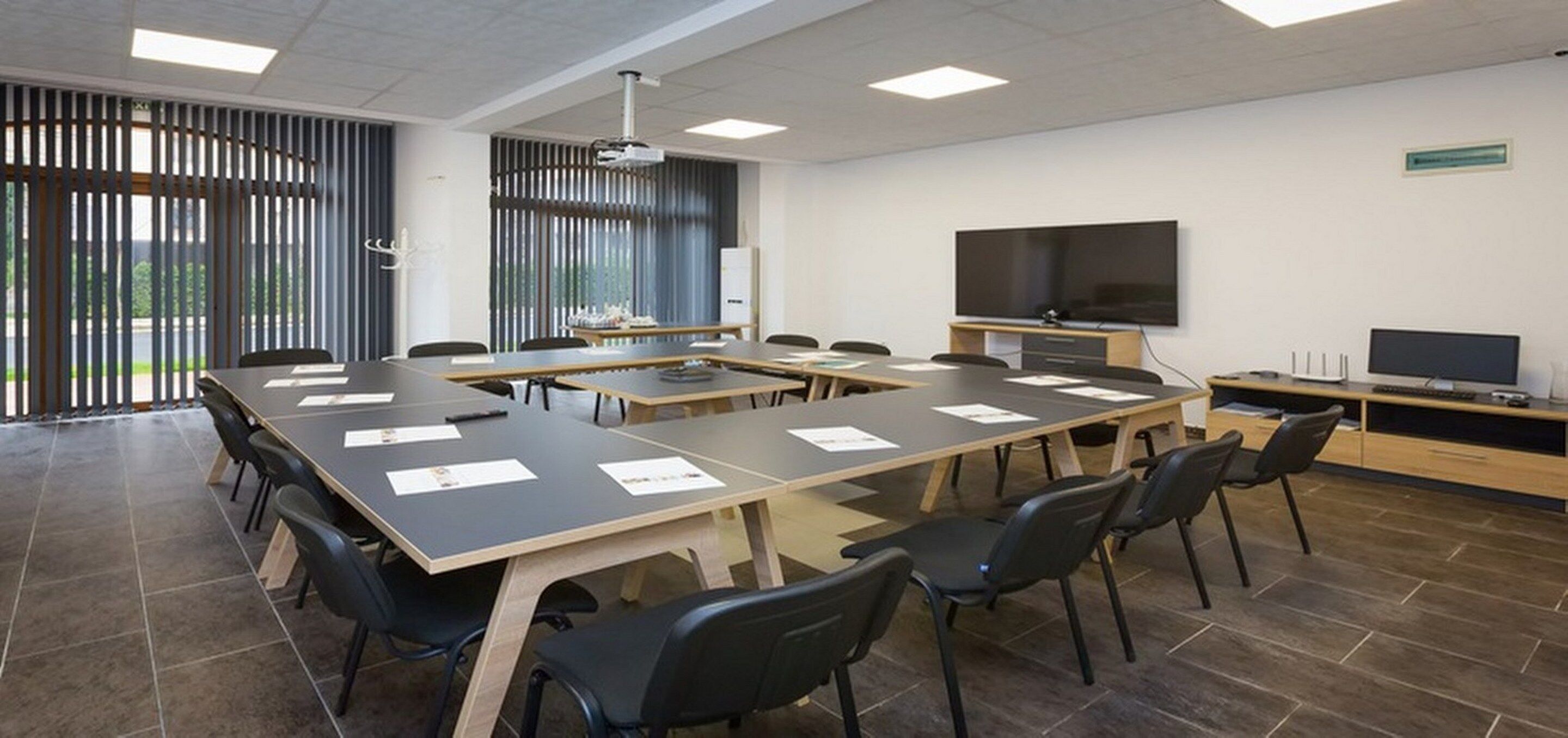 A conference room with a long table, chairs, a projector, a TV, and a whiteboard.