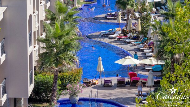 Een resort met een centraal gelegen zwembad, ligbedden, parasols en palmbomen.