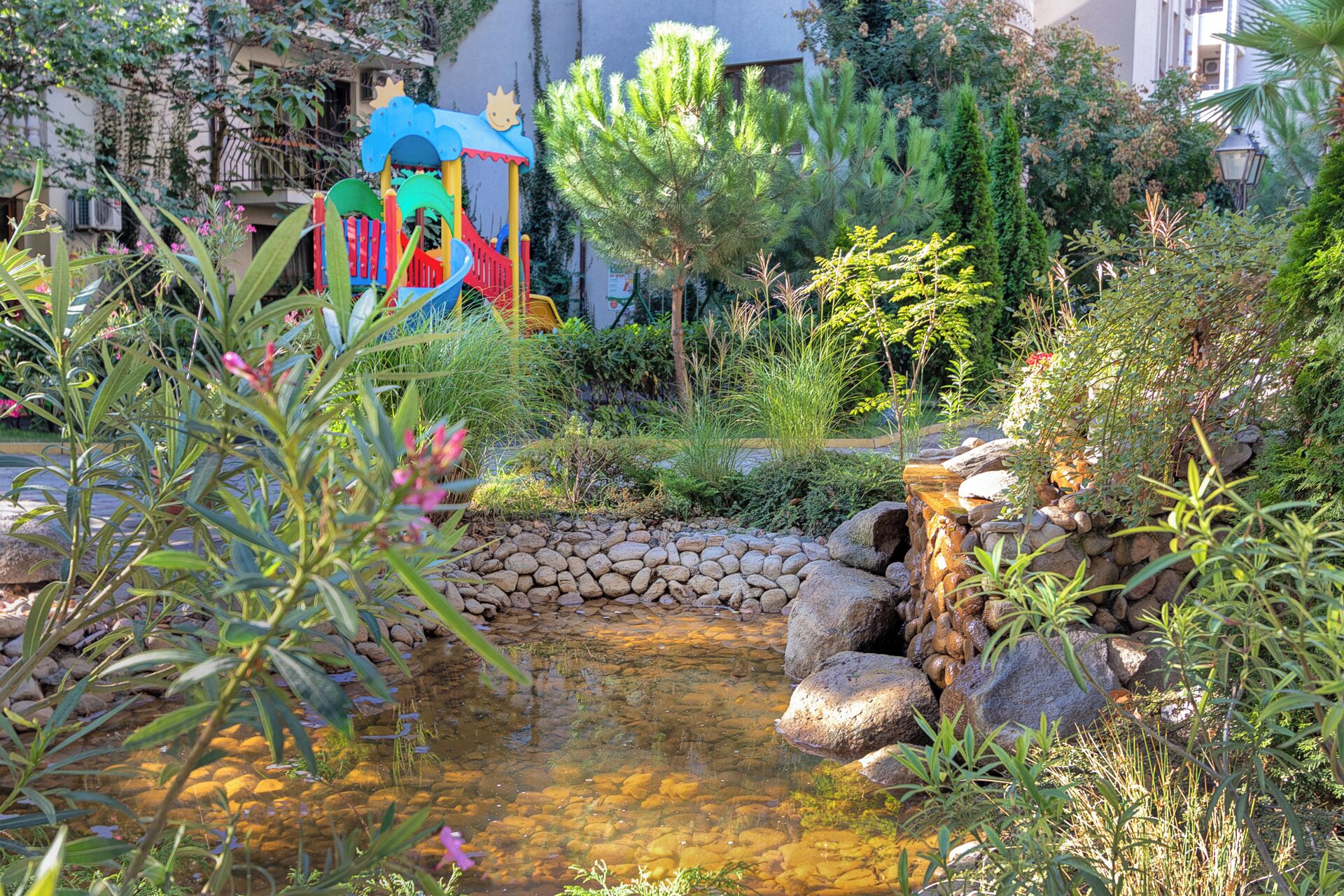 Ein Garten mit Teich, Steinen und einer bunten Spielanlage.