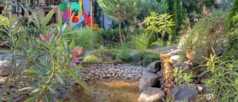 Ein Garten mit Teich, Steinen und einer bunten Spielanlage.