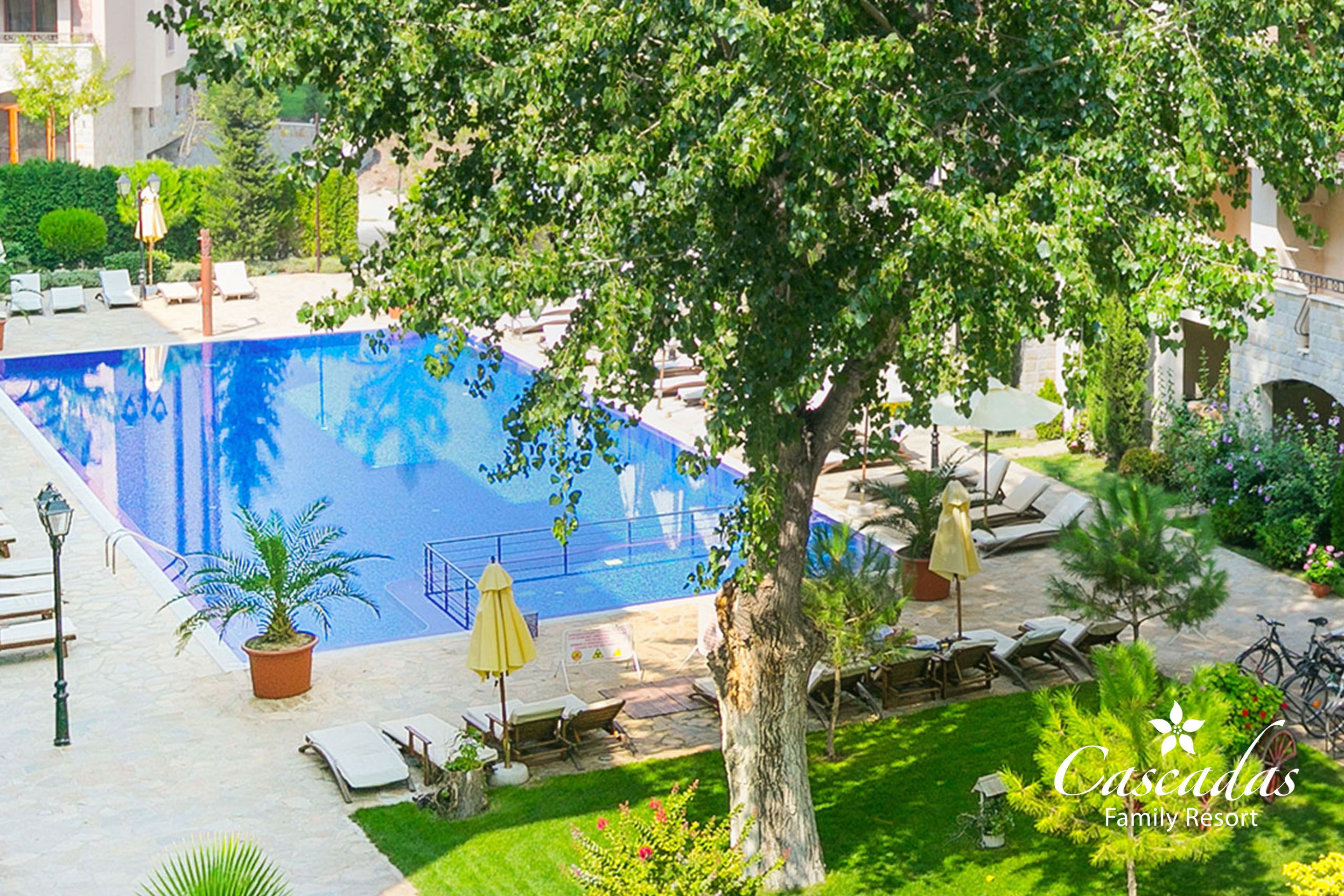 A swimming pool surrounded by lounge chairs, a tree, and a sign for Cascadas Family Resort.
