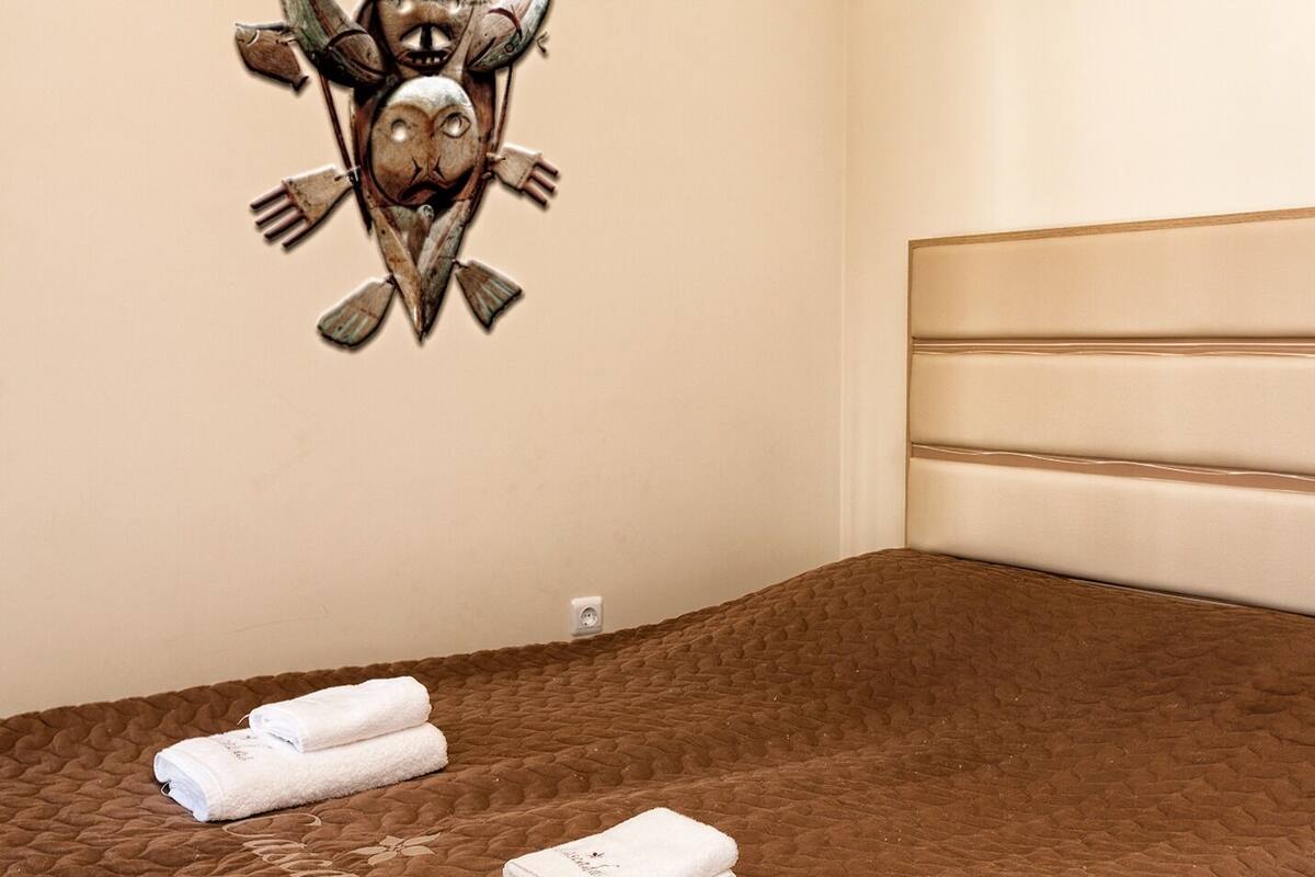 A hotel room with a brown quilted bedspread, a headboard with horizontal panels, and two folded white towels on the bed.