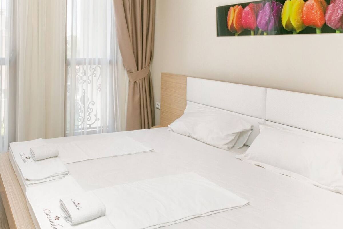 A hotel room with a large bed, white linens, and a painting of tulips on the wall.