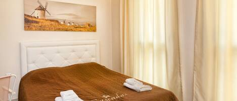 A hotel room with a tufted headboard, a brown bedspread, and a painting of windmills on the wall.