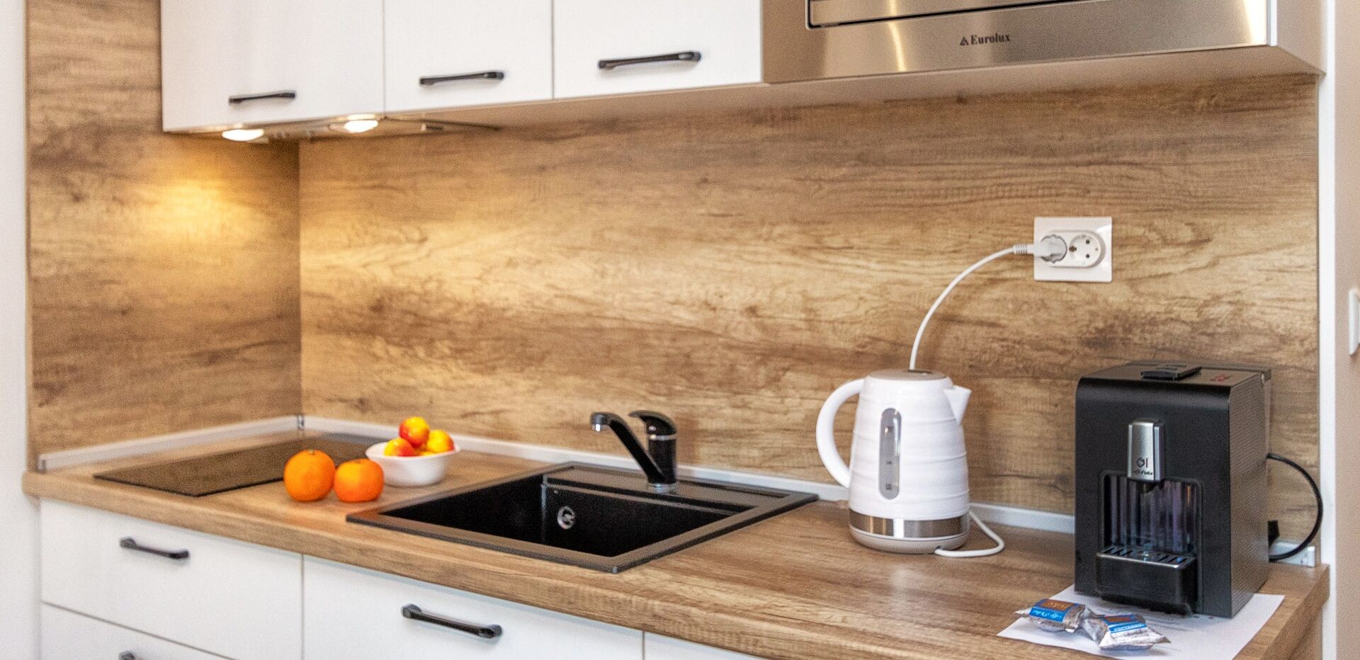 A modern kitchen with a wooden countertop, a sink, a kettle, and a coffee machine.