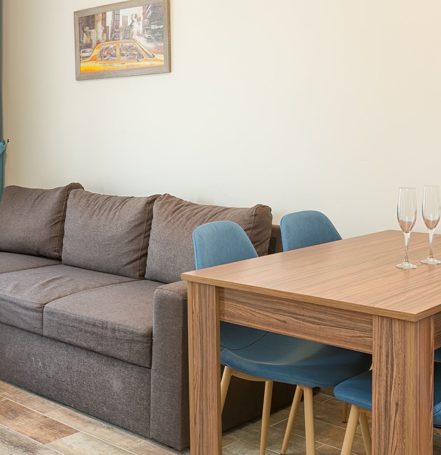 A modern living room with a grey sofa, a wooden dining table with two chairs, and two glasses on the table.