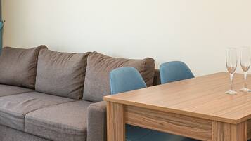 A modern living room with a grey sofa, a wooden dining table with two chairs, and two glasses on the table.
