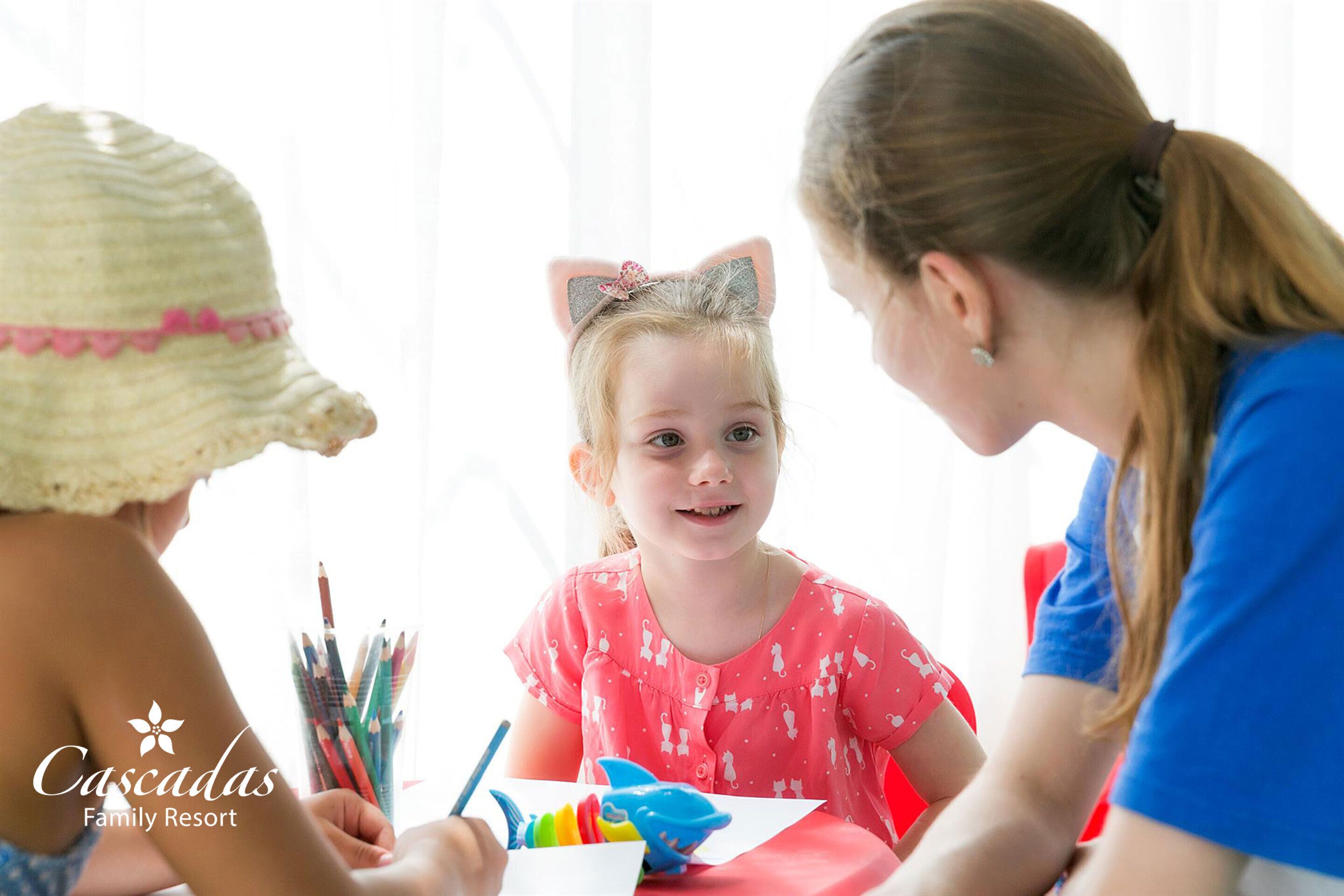 A family at a table with a child drawing, surrounded by colored pencils and a toy shark.