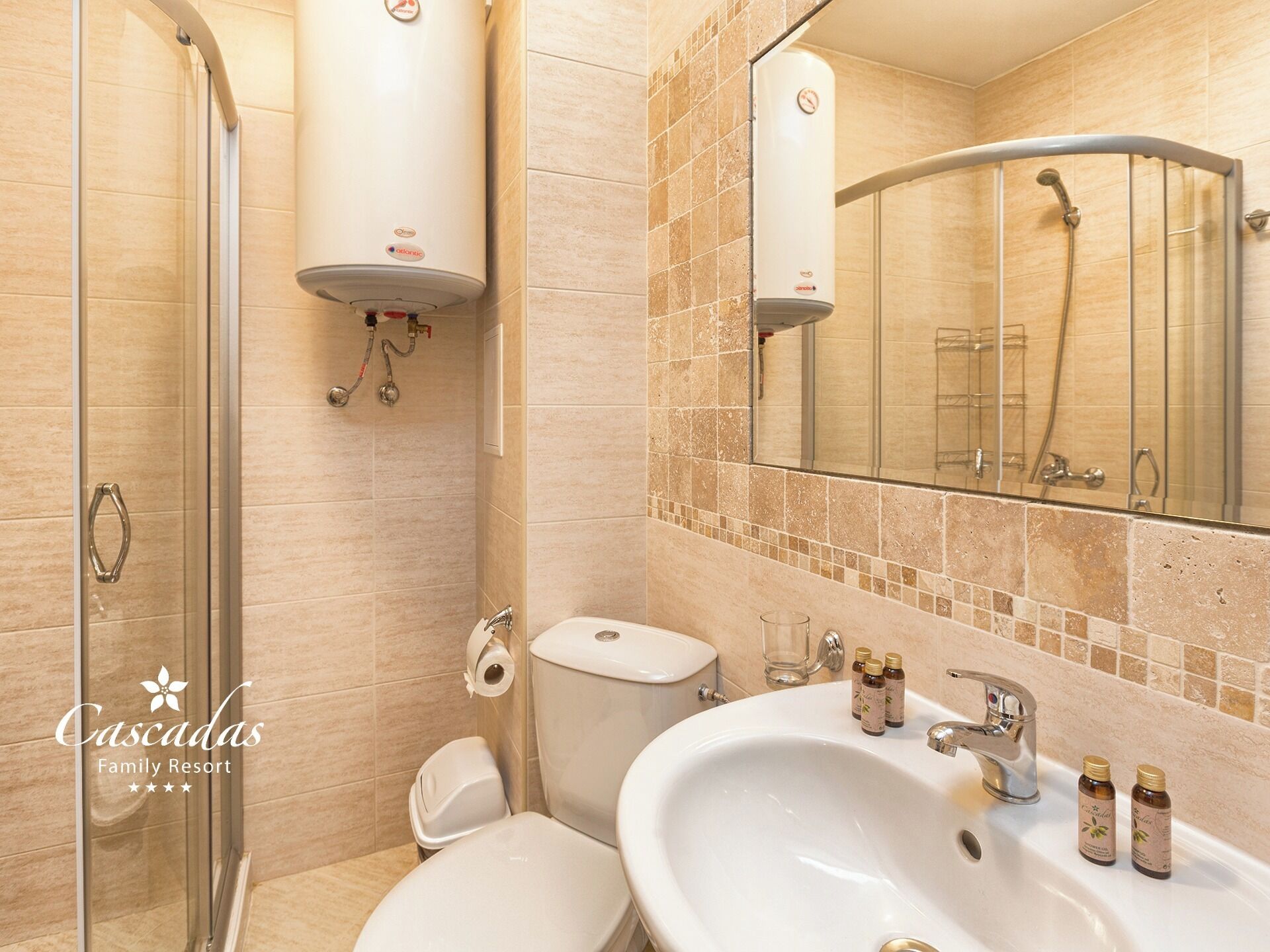 A bathroom with a glass shower enclosure, a toilet, a sink with toiletries, and a mirror.