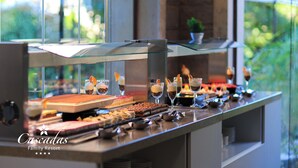 Een buffet met diverse desserts en drankjes, een glazen vitrine en uitzicht op groen buiten.