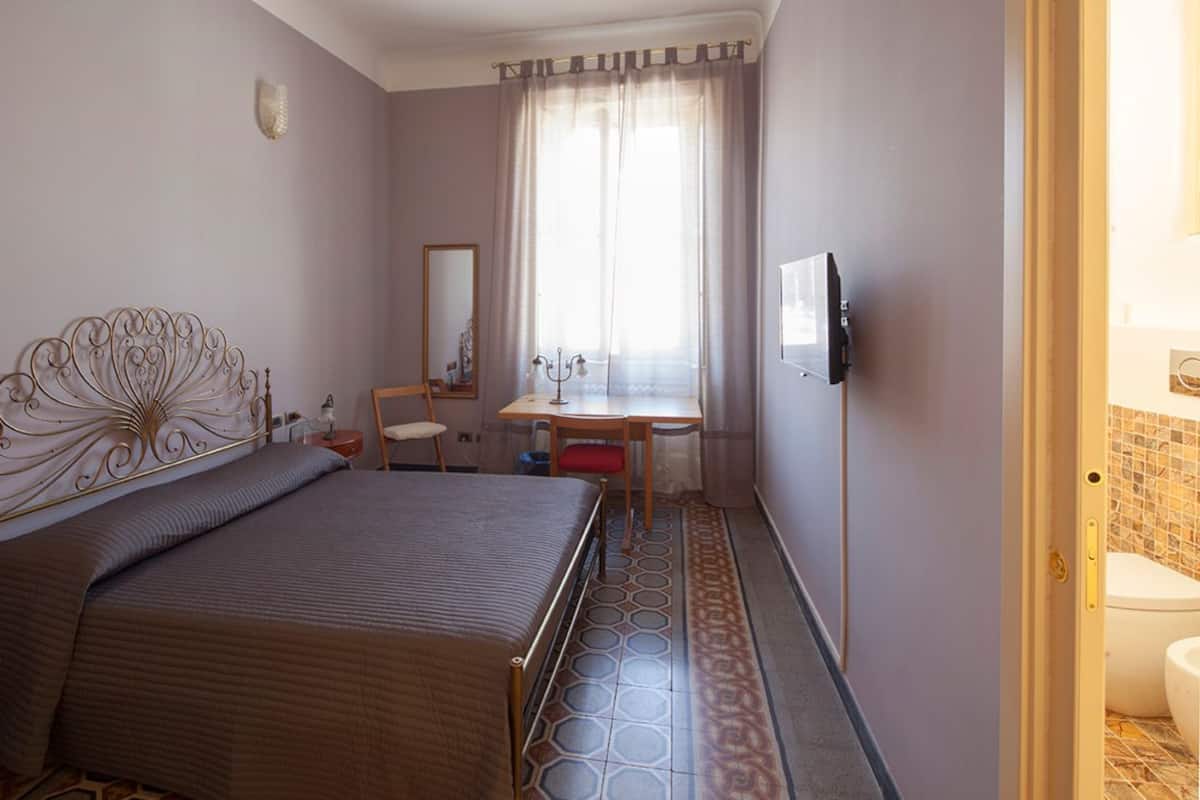 Un dormitorio con cama, escritorio, silla, espejo y un baño visible a través de una puerta abierta.
