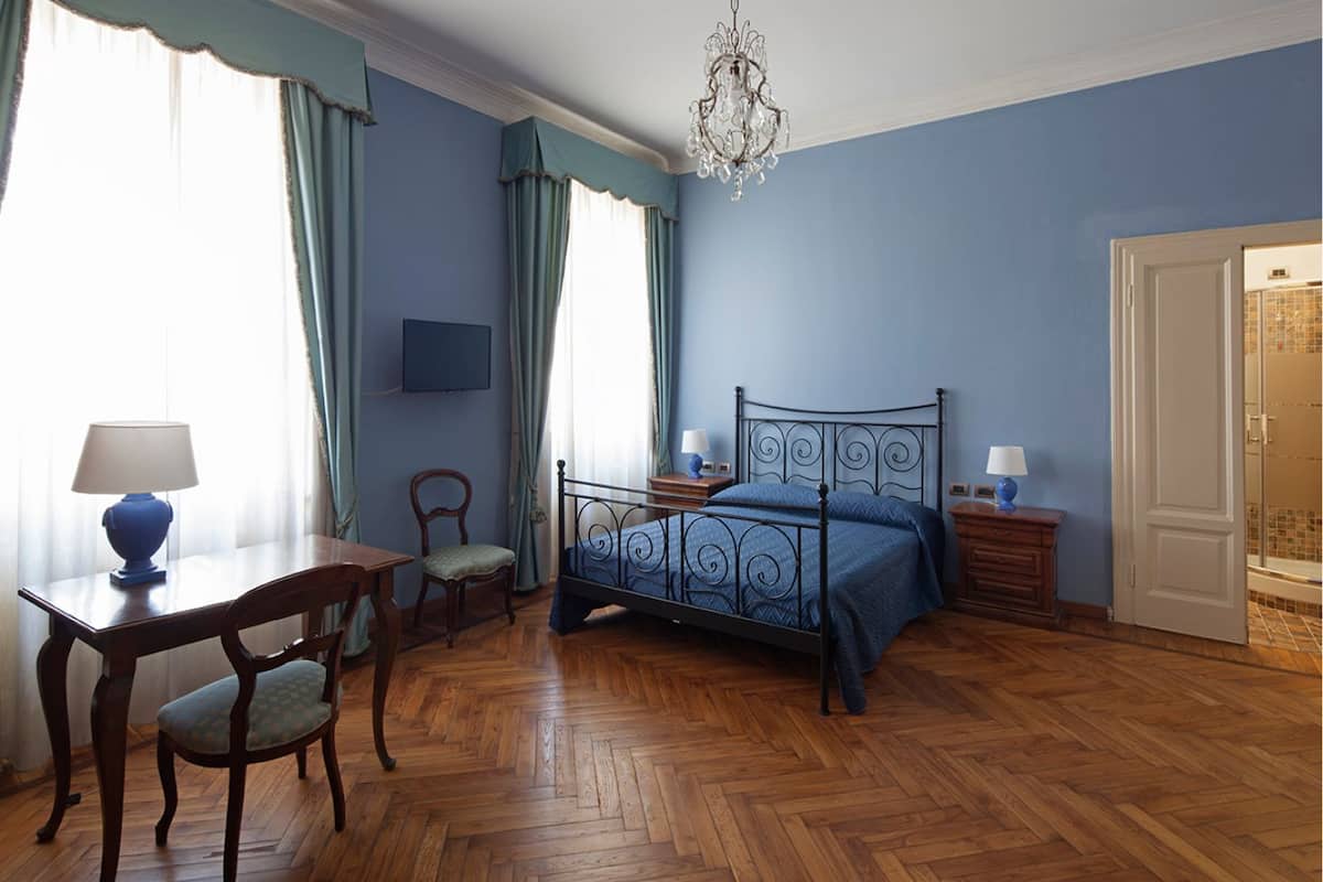Un dormitorio con piso de parqué de madera, estructura de cama metálica, escritorio con lámpara y una silla.