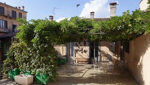 Un patio con una pérgola cubierta de follaje, un banco y mobiliario de exterior.