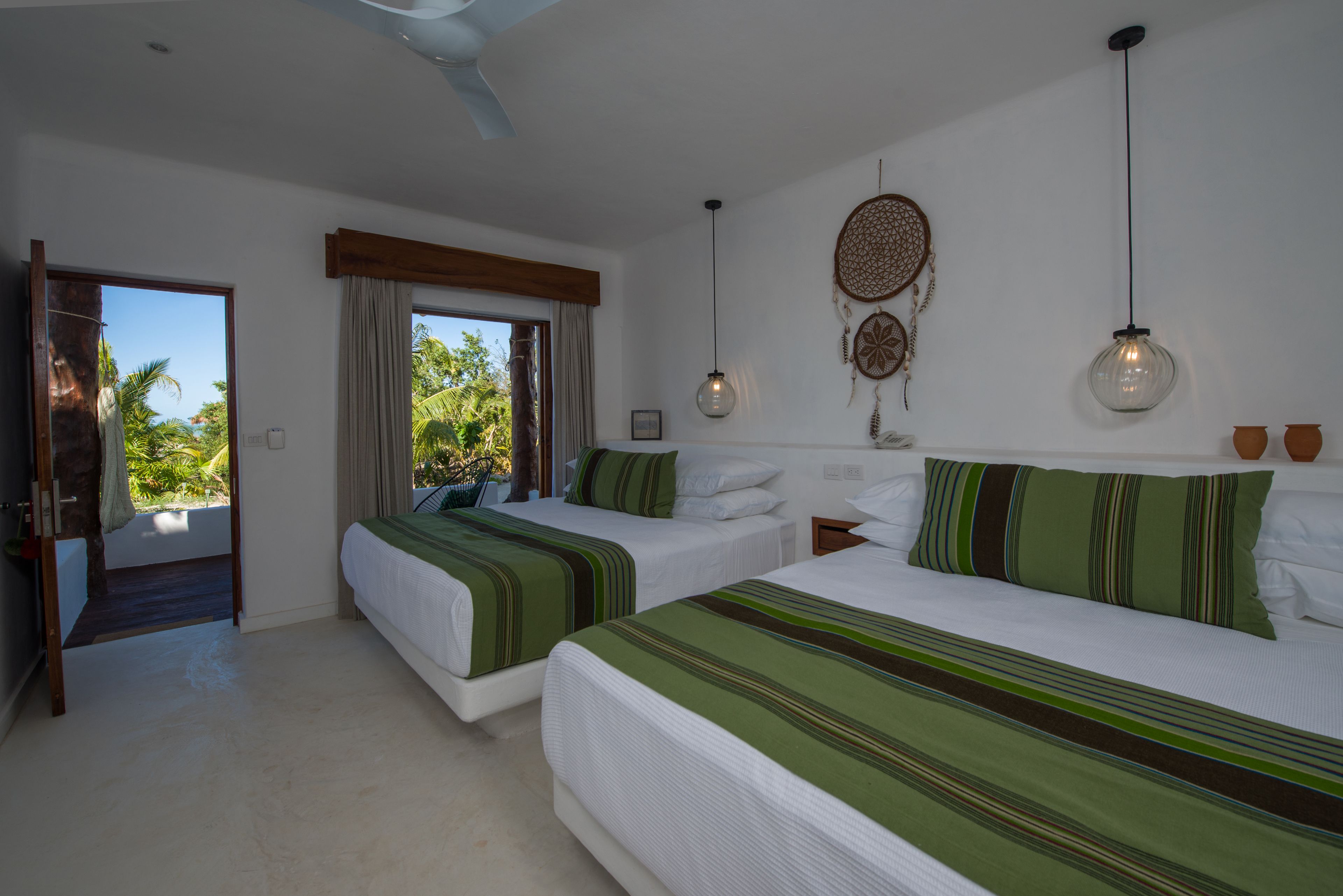 A hotel room with two beds, a large window, a ceiling fan, and a dreamcatcher decoration.