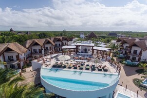 Un resort con piscina central, edificios de techo de paja y vista al océano.