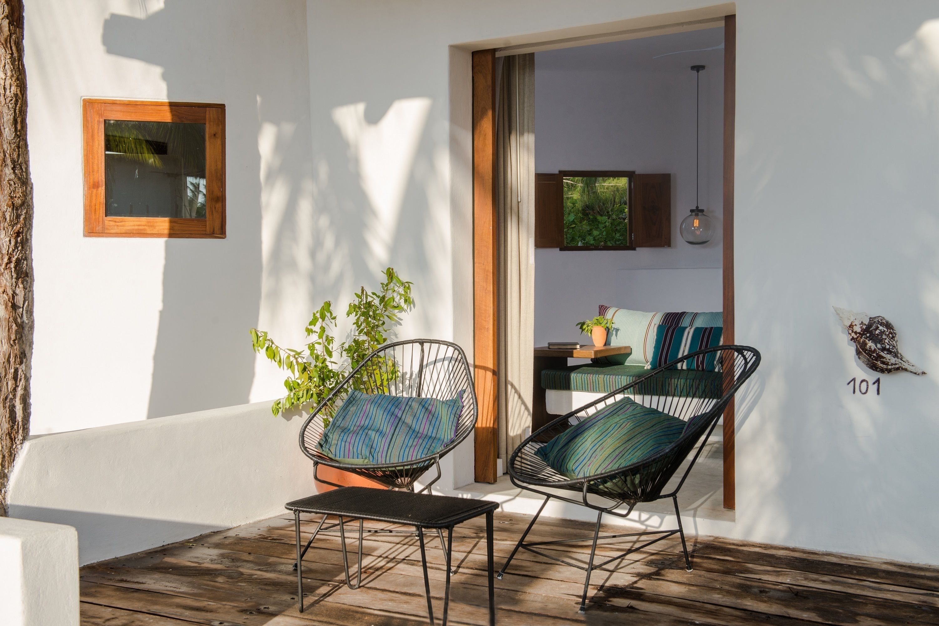 A patio with two black wireframe chairs, a wooden table, and a potted plant.