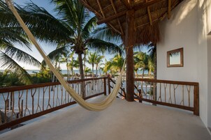 Una hamaca bajo techo de paja, palmeras y vista al mar.