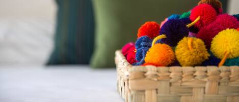 Een mand met kleurrijke pompons op een bed, met een groen kussen op de achtergrond.
