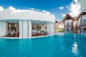 Un resort moderno con una gran piscina, zona de comedor al aire libre y varias construcciones con balcones.