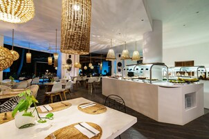 Un área de comedor moderna con lámparas colgantes de mimbre, un mostrador tipo bufé y una piscina al fondo.