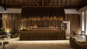 A room with a thatched ceiling, a central bar area with plants and candles, and seating arrangements. - Villas HM Palapas del Mar (Isla Holbox)